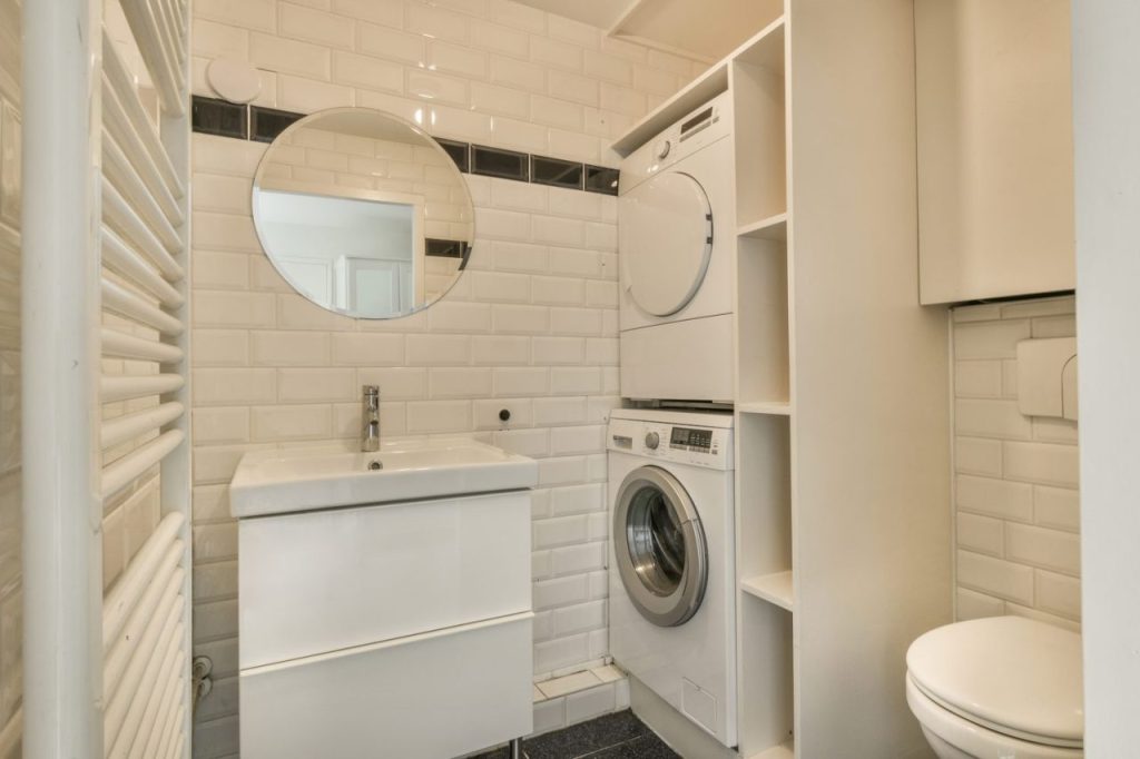 Lave-linge installé dans une petite salle de bain avec des raccordements d’eau sécurisés.